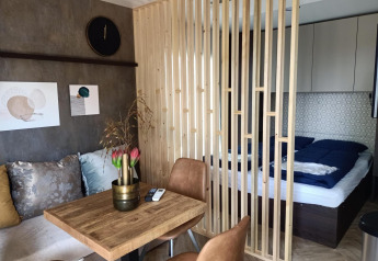 Moderne indretning i et Tiny House med trægitter, soveområde, spisebord og sofa med farverige puder.