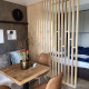 Modern tiny house interieur met houten wand, bedgedeelte, eettafel en decoratieve kussens op de bank.