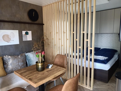 Interior moderno de una tiny house con separador de madera, área de cama, mesa comedor y sofá colorido.