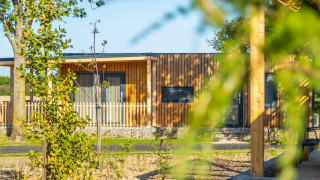 View of a modern wooden lodge at Palisade, surrounded by greenery and trees on a sunny day outdoors.