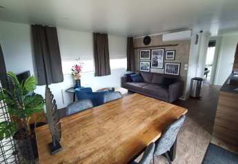 Moderne leefruimte met houten tafel, grijze zetel en wanddecor in Palisade Lodge bij Poort van Maastricht.