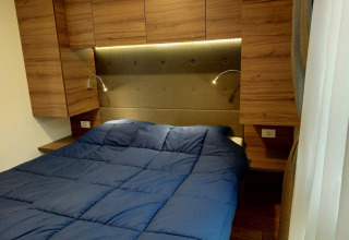 Dormitorio moderno con edredón azul, armarios de madera y lámparas en Palisade en Poort van Maastricht, Países Bajos.