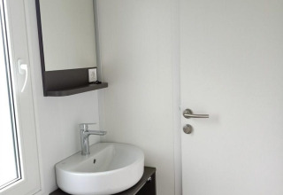 Lavabo moderno con espejo y mueble junto a una puerta blanca en una cabaña de Maastricht, Países Bajos.