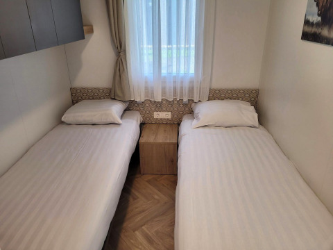 To enkeltsenge i et lyst værelse på lodge Belsano, Poort van Maastricht, Holland, med vindue imellem.