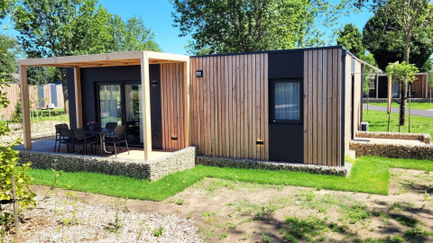 Moderna cabaña de madera Belsano en Poort van Maastricht con terraza, jardín y rodeada de árboles verdes.
