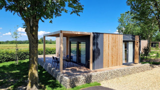 Modern glamping accommodation Domus with wooden facade, outdoor terrace, and seating in natural setting.