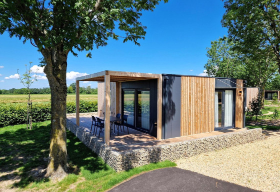 Hébergement glamping moderne Domus avec façade en bois, terrasse extérieure et coin salon en pleine nature.