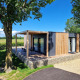 Moderne glamping-indkvartering Domus med træfacade, terrasse og loungeområde i naturlig omgivelser.