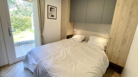 Cozy bedroom at Domus glamping, featuring twin beds, modern design, garden view through a glass door, and wall art.
