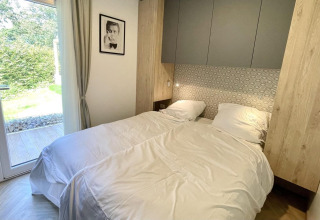 Cozy bedroom at Domus glamping, featuring twin beds, modern design, garden view through a glass door, and wall art.