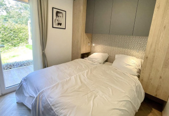 Komfortabelt soveværelse med to senge, moderne indretning, glasdør til have og kunst på væggen i Domus glamping.