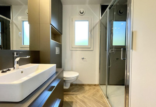 Salle de bain moderne à l’hébergement glamping Domus avec douche, lavabo et toilette lumineuse.