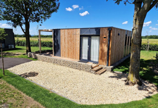 Hébergement glamping Domus moderne avec façade en bois, terrasse en pierre et arbres dans un cadre champêtre.
