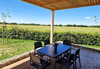 Vue depuis le lodge Domus à Poort van Maastricht, Pays-Bas, avec terrasse, table et chaises devant champ.