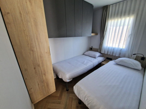 Small bedroom in the Domus tiny house at Poort van Maastricht, Netherlands, with twin beds and window.