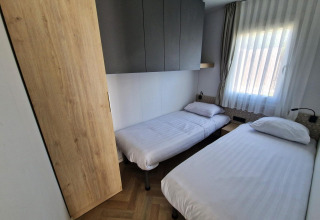 Small bedroom in the Domus tiny house at Poort van Maastricht, Netherlands, with twin beds and window.