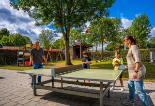 Famille jouant au tennis de table devant une tiny house Domus à Poort van Maastricht, aux Pays-Bas.