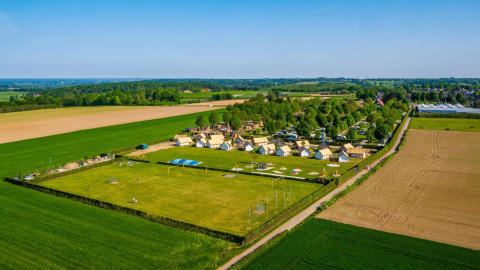 Aerial view of tiny houses and campsite at Poort van Maastricht, Netherlands, surrounded by green fields.