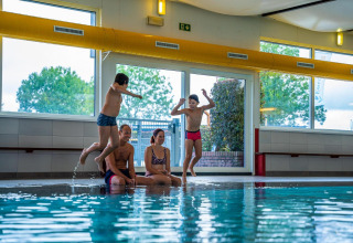 Two kids jump into an indoor pool as two adults sit by the edge at Domus, Poort van Maastricht, Netherlands.