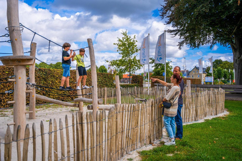 Two kids play on a rope course by the Domus tiny house at Poort van Maastricht, Netherlands, as adults watch.