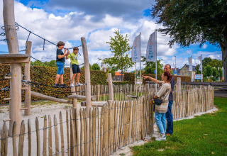 Two kids play on a rope course by the Domus tiny house at Poort van Maastricht, Netherlands, as adults watch.