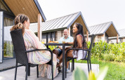 Three people enjoy a meal outside the Mountain Lodge at Resort Mooi Bemelen in the Netherlands, surrounded by greenery.