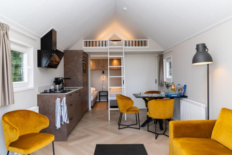 Modernes Mountain Lodge im Resort Mooi Bemelen, Niederlande, mit gelben Stühlen und Schlafempore.