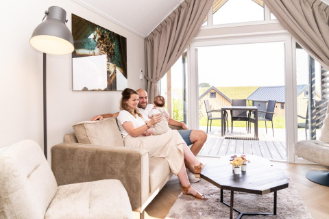 Een gezin zit gezellig in de woonkamer van Mountain Lodge op Resort Mooi Bemelen in Nederland.