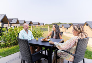 Tres personas disfrutan del desayuno al aire libre en una mesa cerca de cabañas en Mountain Lodge, Resort Mooi Bemelen, Países Bajos.