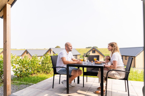 Familie frühstückt draußen an einem Tisch im Mountain Lodge, Resort Mooi Bemelen, mit Blick auf Chalets.