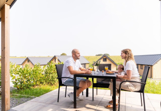 Gezin geniet van ontbijt buiten aan Mountain Lodge bij Resort Mooi Bemelen, Nederland, met lodges op de achtergrond.