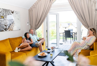 Tre personer slapper af på gule sofaer i Mountain Lodge på Resort Mooi Bemelen i Holland.