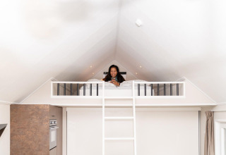 Mujer relajándose en la cama altillo de Mountain Lodge en Resort Mooi Bemelen, Países Bajos, ambiente acogedor.