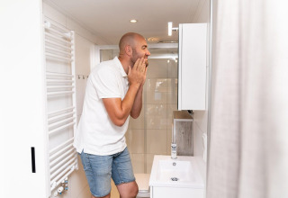 Hombre con camiseta polo blanca mira su cara en el baño de Mountain Lodge en Resort Mooi Bemelen, Países Bajos.
