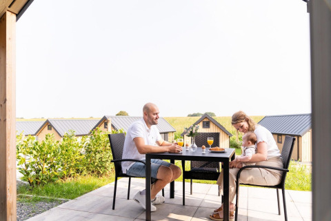 Familie frühstückt draußen an der Mountain Lodge, Resort Mooi Bemelen, Niederlande, mit Hütten im Hintergrund.