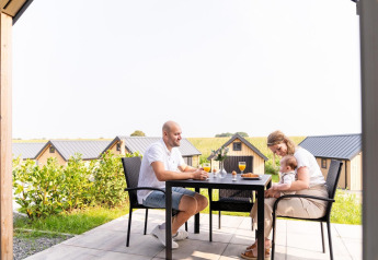 Familie frühstückt draußen an der Mountain Lodge, Resort Mooi Bemelen, Niederlande, mit Hütten im Hintergrund.