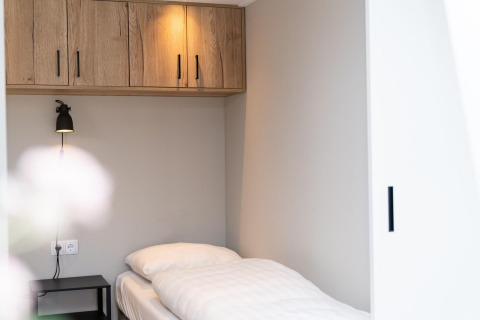 Einzelbett mit weißer Bettwäsche und Holzschränken im Mountain Lodge im Resort Mooi Bemelen, Niederlande.
