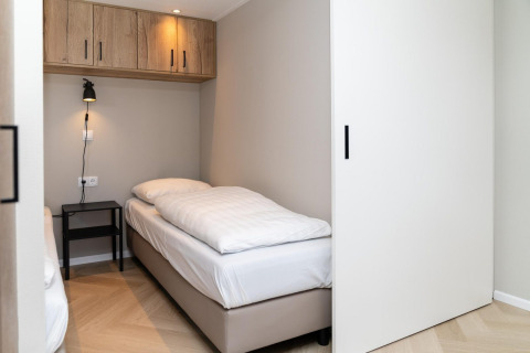 Modernes Einzelbett mit weißer Bettwäsche, Nachttisch und Wandleuchte im Mountain Lodge, Resort Mooi Bemelen.