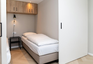 Letto singolo moderno con lenzuola bianche, comodino e lampada a muro al Mountain Lodge, Resort Mooi Bemelen, Paesi Bassi.