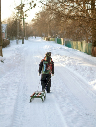 Een kind trekt een slee over een besneeuwde weg in een vakantiepark met glamping accommodaties.