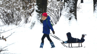 Un enfant tire un autre enfant sur une luge à travers un paysage d'hiver enneigé et arboré.