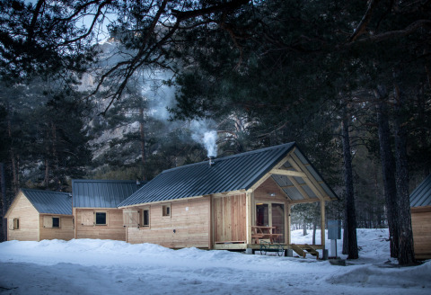 Cabañas de madera con humo de la chimenea en un bosque nevado en Huttopia la Clarée, Provenza-Alpes-Costa Azul.