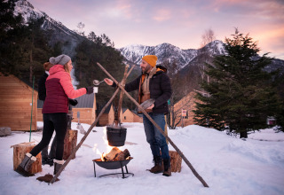 Menschen genießen ein Lagerfeuer im Schnee bei Hütten von Huttopia la Clarée in Provence-Alpes-Côte d’Azur.