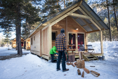Dos personas fuera de un chalet de madera en la nieve en Huttopia la Clarée, parque vacacional en Provenza-Alpes-Costa Azul.