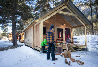 Twee mensen bij een houten chalet in de sneeuw aan Huttopia la Clarée, vakantiepark in Provence-Alpes-Côte d’Azur.