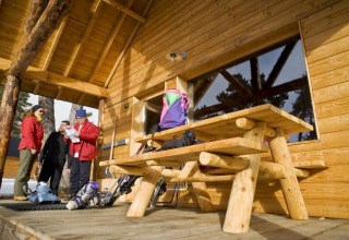 Gruppe vor einer Holzhütte mit Skiausrüstung und Picknicktisch im Les Chalets Huttopia de Font-Romeu, Frankreich.
