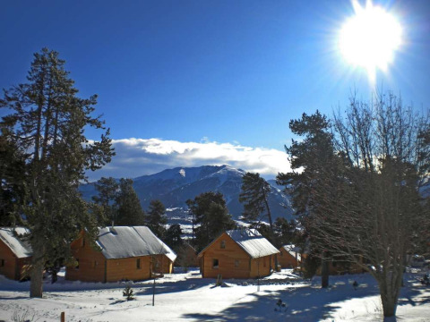 Cabañas de madera cubiertas de nieve en Les Chalets Huttopia de Font-Romeu, Occitania, Francia, bajo un cielo soleado.