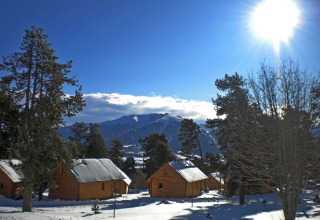 Chalets en bois recouverts de neige à Les Chalets Huttopia de Font-Romeu, Occitanie, France, sous un ciel ensoleillé.