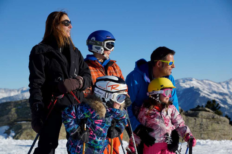 Gezin geniet van skiën bij Les Chalets Huttopia de Font-Romeu, omgeven door besneeuwde bergen.