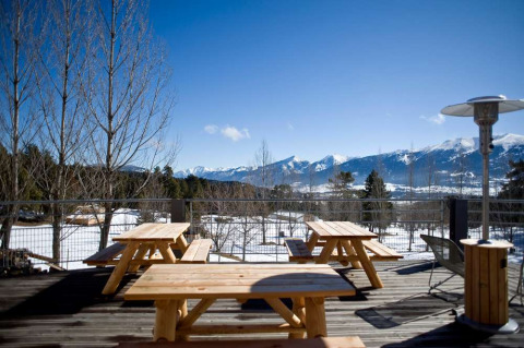 Mesas de madera en una terraza con impresionantes vistas a las montañas nevadas en Huttopia Font-Romeu, Francia.